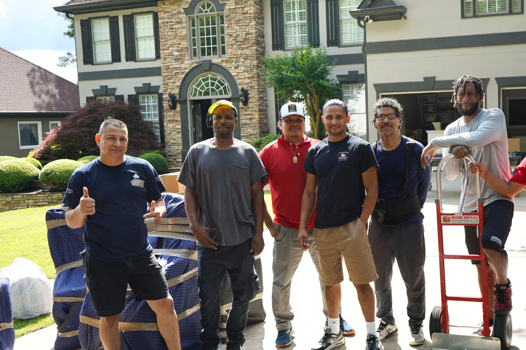 Professional moving team from Atlanta Pack & Load posing outside a home, showcasing their expertise in relocation services with moving supplies and equipment.