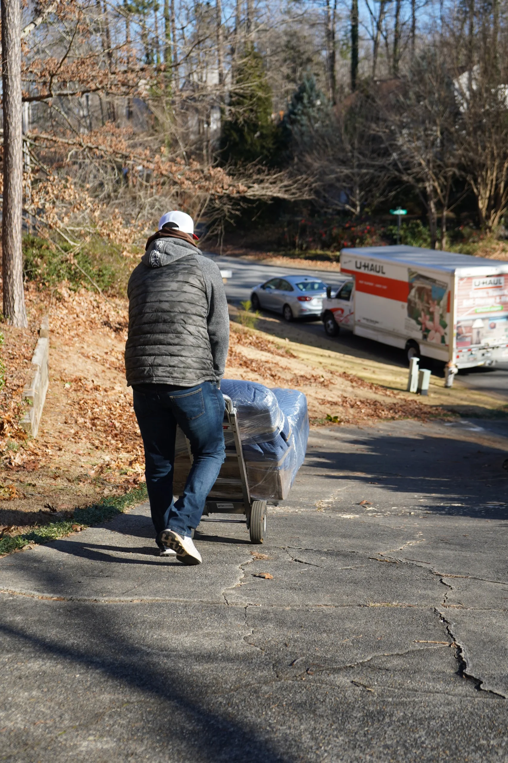 Man pushing a dolly with wrapped furniture down a driveway, U-Haul truck parked nearby, showcasing professional moving and donation services in Austell, GA.