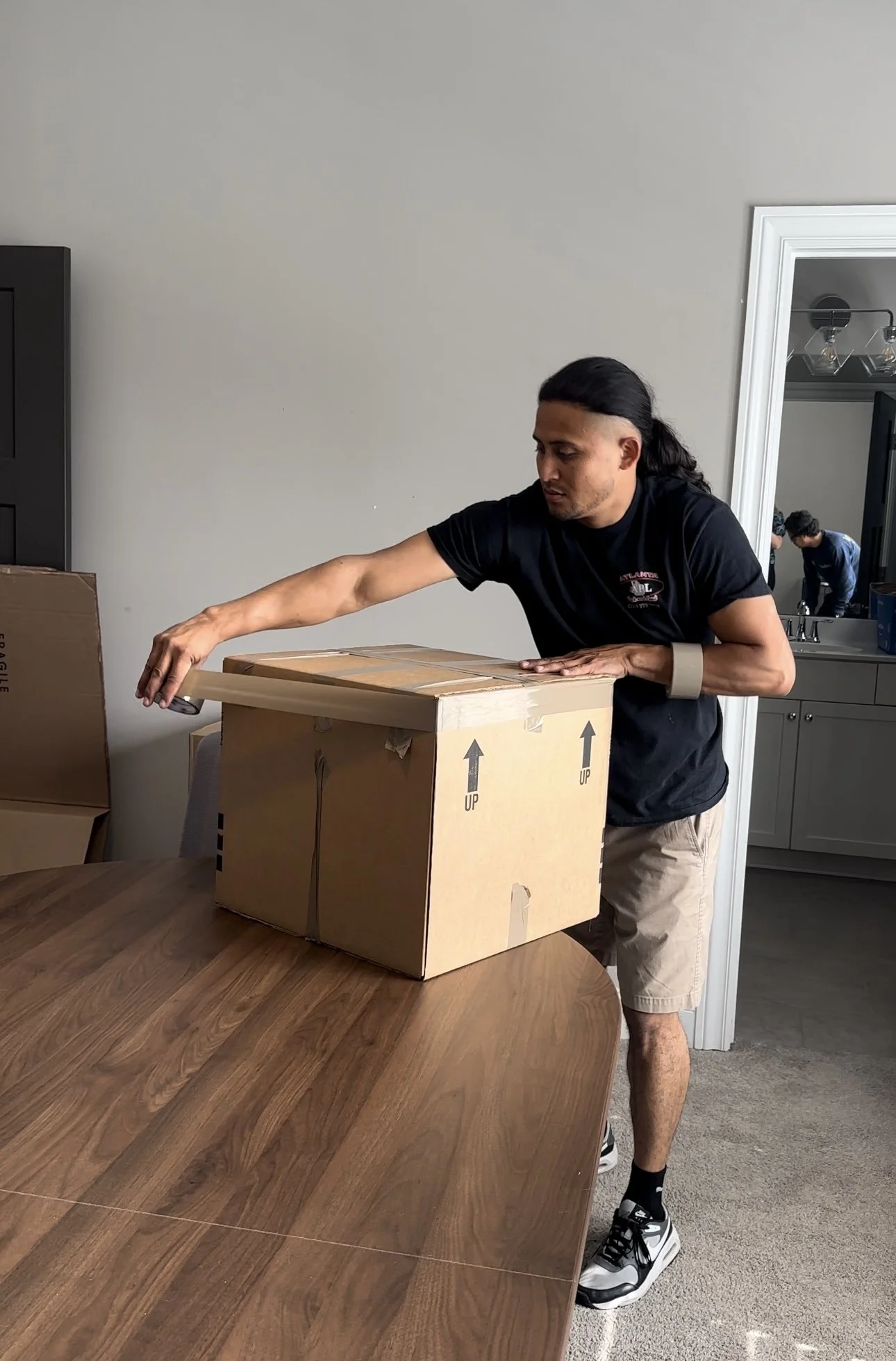 Man packing a cardboard box with labels indicating "UP," demonstrating professional moving services for commercial clients in a well-organized workspace.