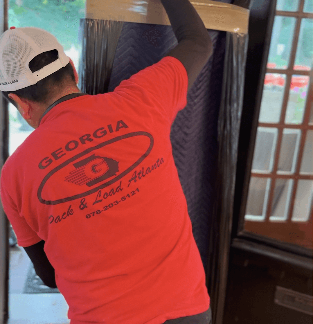 Worker in red shirt with "Georgia Pack & Load Atlanta" logo, wrapping furniture for donation or disposal, showcasing Atlanta Pack and Load's decluttering services in Metro Atlanta.