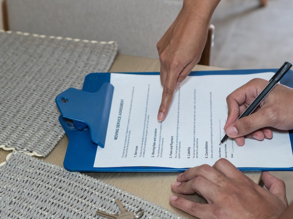 Hands reviewing and signing a moving service agreement on a clipboard, emphasizing the importance of moving insurance for long distance relocation.