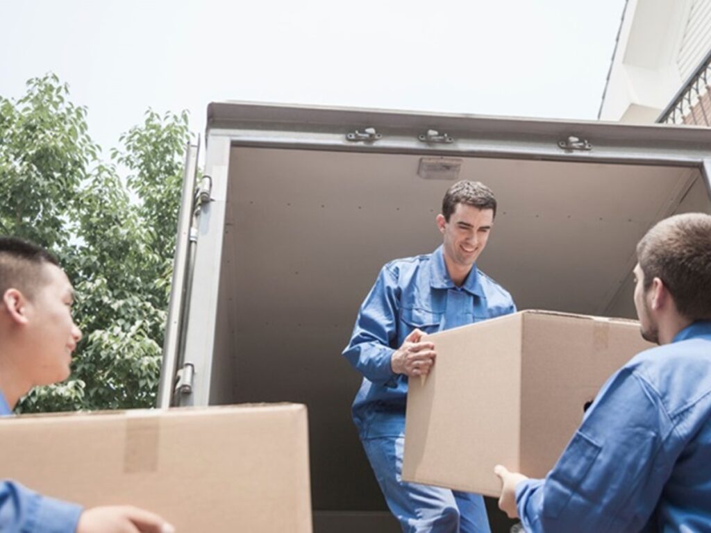 Movers in blue uniforms loading boxes into a truck, emphasizing the logistics of long-distance moving and the importance of insurance coverage during transit.