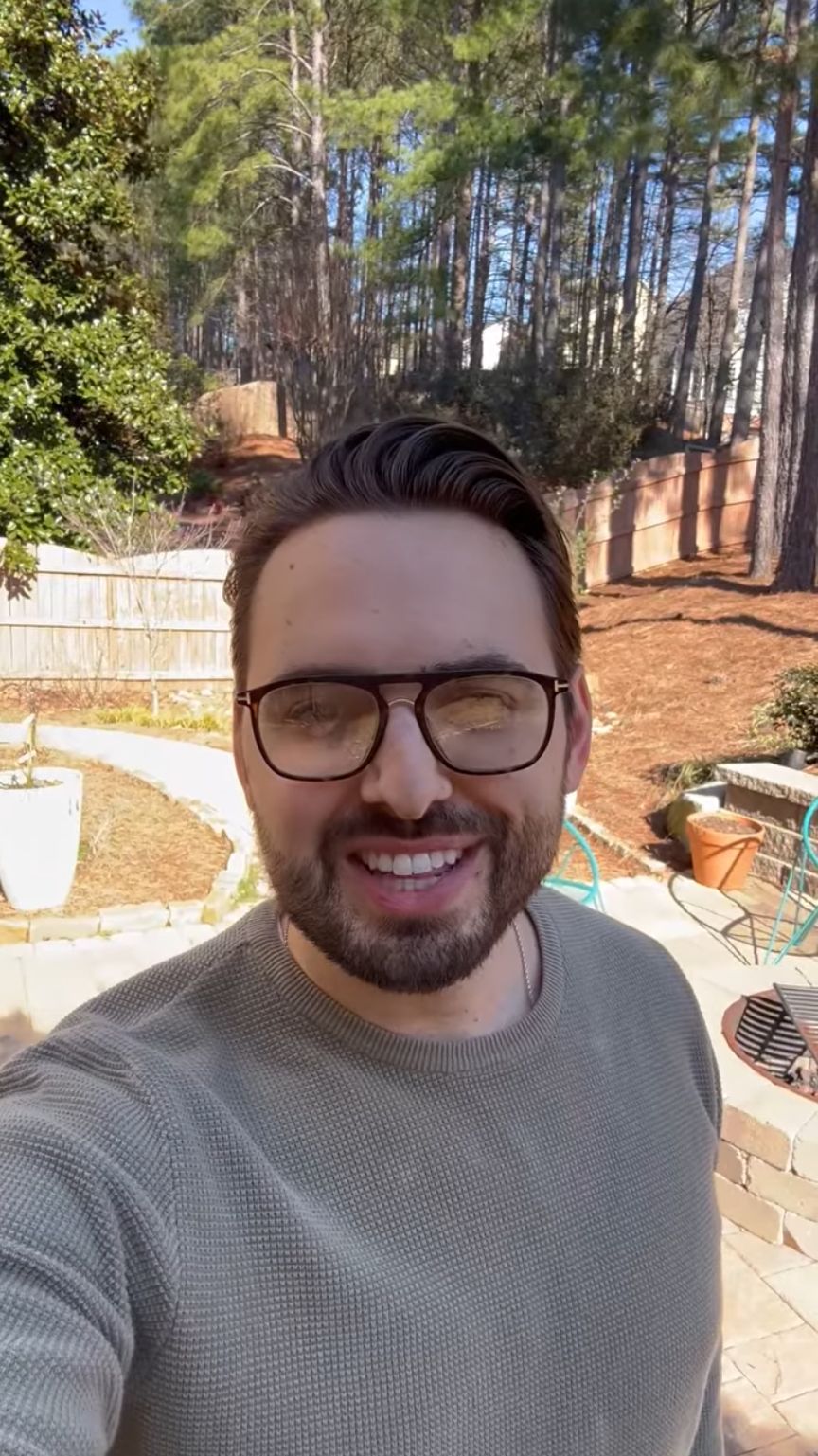 Smiling man in a casual sweater, standing in a backyard with trees and patio furniture, promoting Atlanta Pack and Load's moving services.
