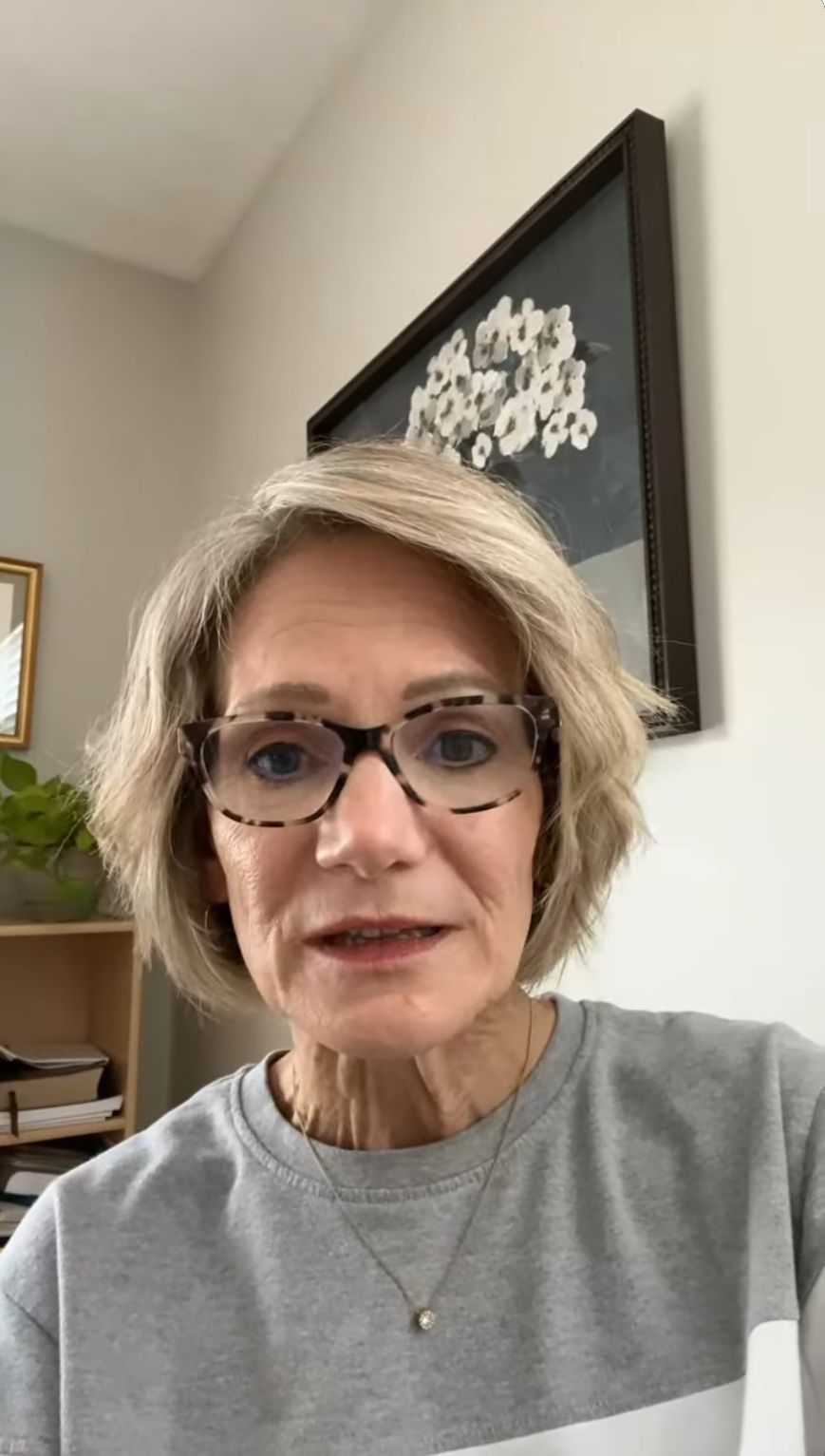 Woman speaking in a casual setting, wearing glasses and a gray sweatshirt, with a plant and framed artwork in the background, reflecting customer satisfaction with Atlanta Pack and Load's moving services.