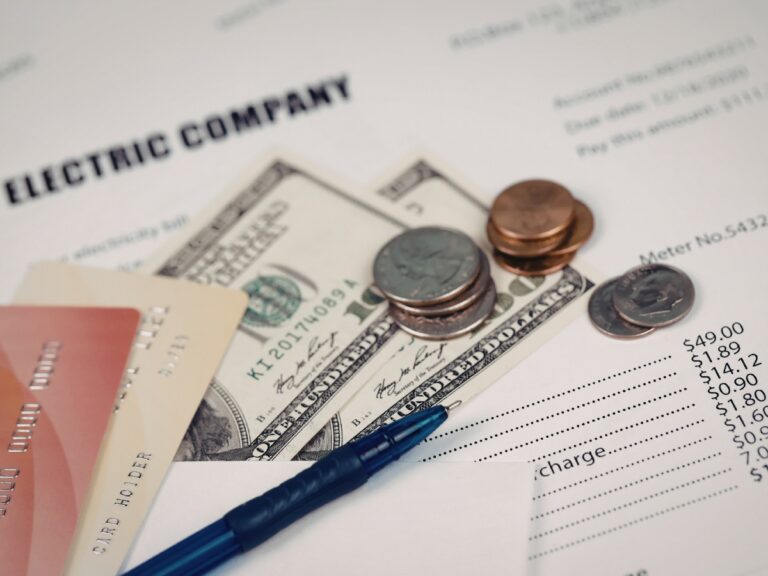 An electric bill with cash, coins, credit cards, and a pen placed on top, highlighting the urgency of payment to avoid utility disconnection.