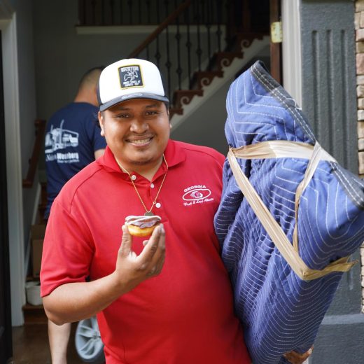 Smiling mover in red shirt holding a packing blanket and a cupcake, ready for a stress-free move, with a staircase in the background.