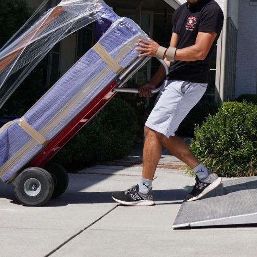 Moving professional transporting wrapped furniture on a hand truck, demonstrating local moving services in Austell, GA.