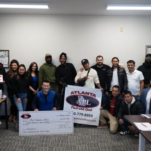 Team members of Atlanta Pack and Load celebrating community involvement, holding a large check and banner with company logo, showcasing teamwork and commitment to service.