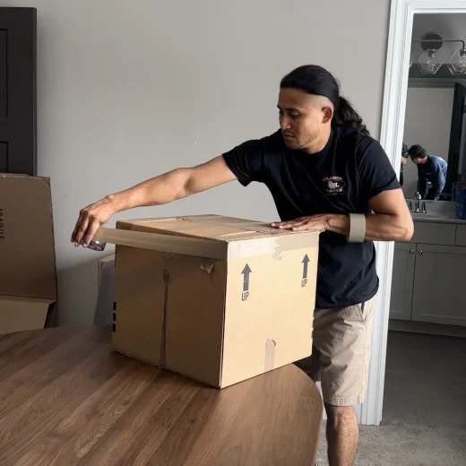 Person preparing a cardboard box for packing, demonstrating professional packing services for long-distance moving, with a focus on secure loading and organization.