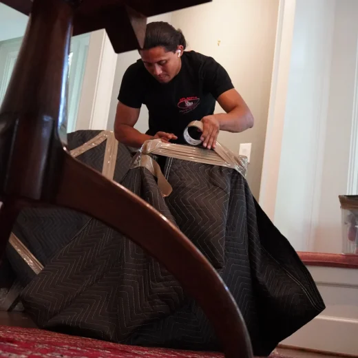 Mover securely wrapping furniture with packing tape in preparation for a stress-free relocation, reflecting Atlanta Pack & Load's professional packing services.