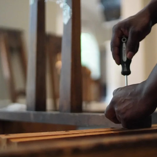 Person using a screwdriver to assemble furniture in a home setting, emphasizing careful handling and preparation for a move.
