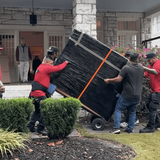 Team of movers transporting a large, securely wrapped item on a dolly, showcasing professional moving services in a residential setting, relevant to Atlanta Pack and Load's local moving and packing offerings.